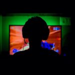 pc game player with headset in silhouette backlit by green wall and red glow from great gaming computer
