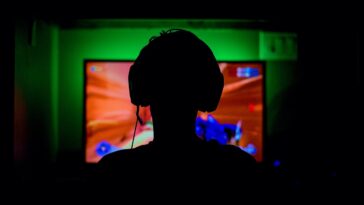 pc game player with headset in silhouette backlit by green wall and red glow from great gaming computer