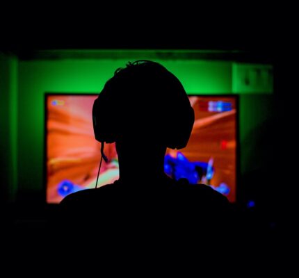pc game player with headset in silhouette backlit by green wall and red glow from great gaming computer